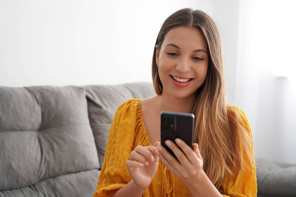 Spaanse aantrekkelijke jonge vrouw met behulp van haar smartphone zitten in haar woonkamer - Foto, afbeelding