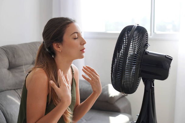 Yaz sıcağı. Genç İspanyol kadın evde solunum cihazıyla serinliyor, sıcak havalarda yüksek sıcaktan rahatsız oluyor. Aşırı sıcak hava dalgası sırasında elektirikli yelpazenin önündeki Latin kız. - Fotoğraf, Görsel