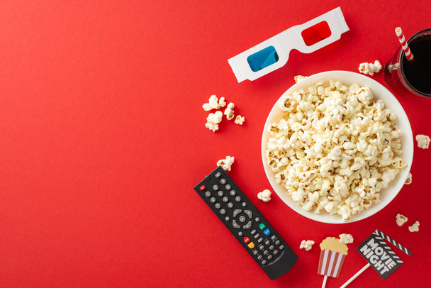 Enjoy premieres on TV app at home. Top view of popcorn, soda, 3D glasses, remote control, and themed decor for party. Red background with space for text or advertising - Photo, Image