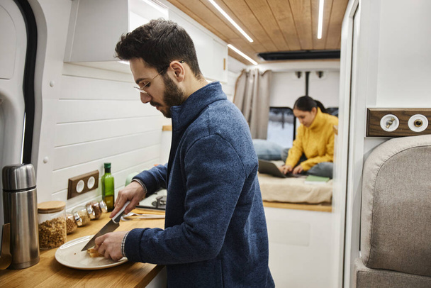 Portrait latéral du jeune homme barbu cuisinant le dîner dans une caravane profitant de la vie sur la route - Photo, image