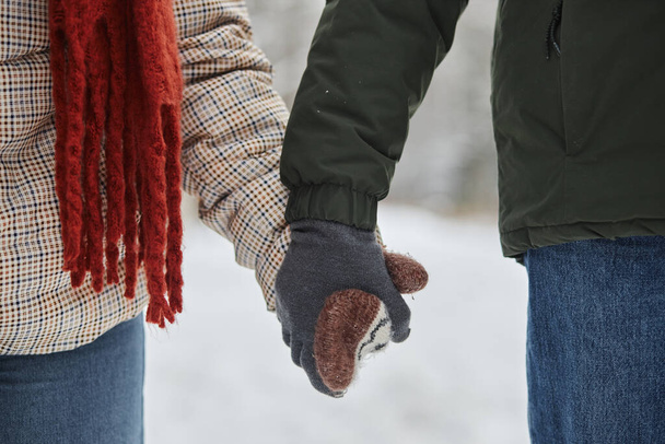 Zbliżenie młodej pary trzymającej się za ręce zimą w uroczych rękawiczkach z dzianin, przestrzeń na ksero - Zdjęcie, obraz