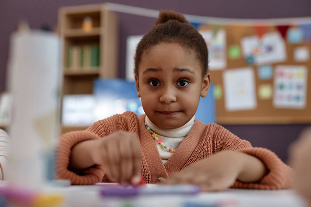 Lähikuva muotokuva söpö Musta tyttö väritys pöydässä taiteen ja käsityön luokan esikoulussa ja katsot kameraa - Valokuva, kuva