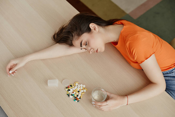 錠剤と錠剤の山で自宅でテーブルに横たわっている落ち込んだ若い女性のトップビュー,コピースペース - 写真・画像