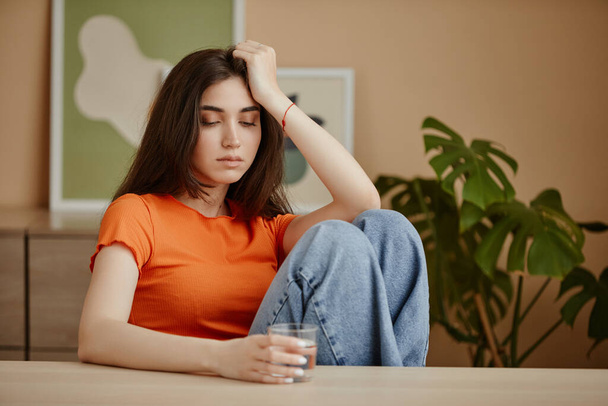 Portrait of depressed young woman holding glass of water struggling with mental health issues, copy space - Photo, Image