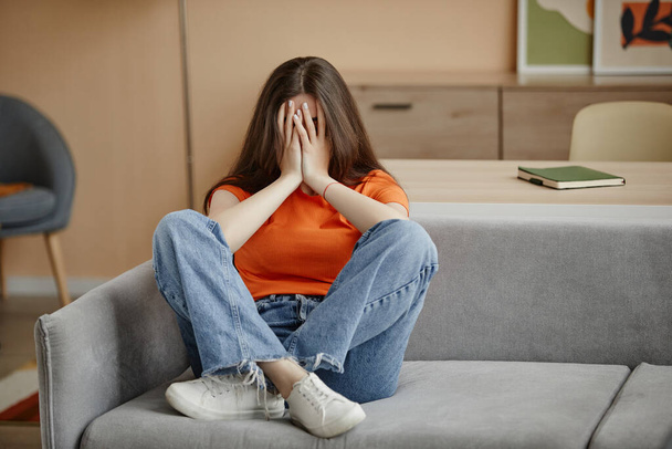 Täyspitkä muotokuva itkevä nuori nainen istuu sohvalla yksin kotona ja kärsii mielenterveysongelmista, kopioi tilaa - Valokuva, kuva