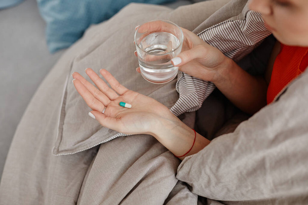 Vista superior primer plano de mujer joven sosteniendo píldora y vaso de agua envuelto en manta, espacio de copia - Foto, imagen
