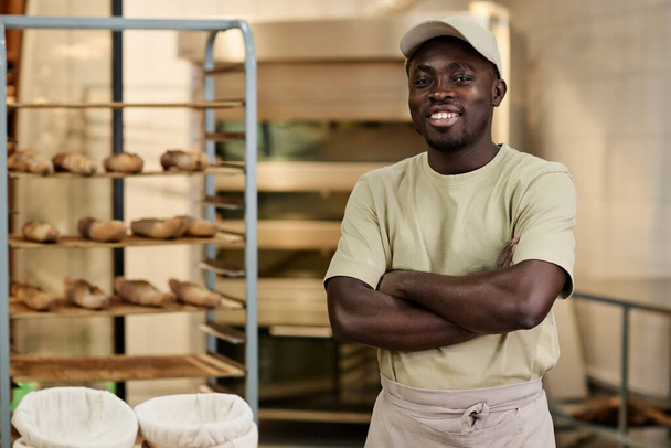 Талия портрет Черного молодого человека, стоящего в пекарне кухня с руками скрестив и улыбаясь в камеру, копировать пространство - Фото, изображение