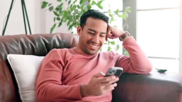 Handy, Lächeln und der Mann auf dem Sofa zu Hause vernetzen sich über soziale Medien, Handy-App oder Internet. Glückliche, tippende und männliche Person scrollen am Telefon mit Online-Website im Wohnzimmer einer modernen Wohnung - Filmmaterial, Video