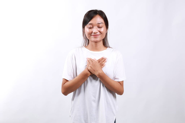 Asiatique jeune femme souriant avec les mains sur la poitrine avec les yeux fermés et geste reconnaissant sur fond blanc, se sent soulagé - Photo, image