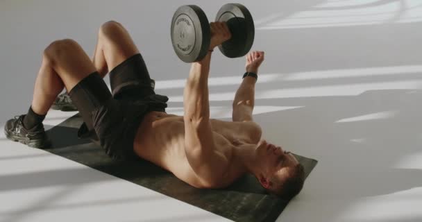 Athletic Young Man Training in Studio with Dumbbells and Focus. Athletic man in a fitness studio training with dumbbells, showcasing strength and concentration. - Footage, Video