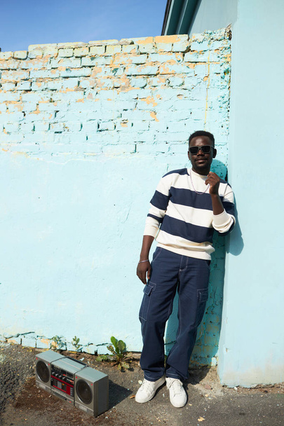 Живой полноразмерный портрет фанки Черного человека, смотрящего на камеру за стеной в городской обстановке - Фото, изображение