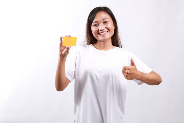 Joven mujer asiática en ropa casual mostrando tarjeta en blanco y el pulgar hacia arriba gesto, aprobar y recomendar, sonriendo a la cámara, fondo blanco - Foto, Imagen