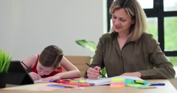 Ελκυστική μητέρα και μικρή κόρη ζωγραφίζουν σε χαρτί με χρωματιστά μολύβια. Η αγαπημένη οικογένεια απολαμβάνει την επικοινωνία και το κοινό δημιουργικό χόμπι - Πλάνα, βίντεο