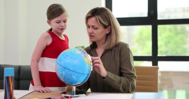 Mère et fille font des devoirs de géographie avec globe à la maison. Professeur montre la carte du monde sur le globe à écolière - Séquence, vidéo