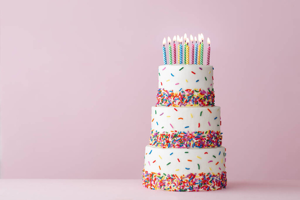 Viering verjaardagstaart met kleurrijke suikerhagelslag en twaalf verjaardagskaarsen - Foto, afbeelding