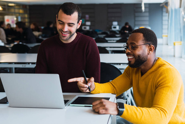 Glimlachende multiraciale bebaarde partners werken samen aan project aan tafel met laptop en tablet in coworking center - Foto, afbeelding