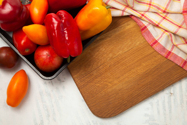 Groente achtergrond afbeelding. Schaal met groenten op snijplank met assort van verschillende hele rijpe sappige tomaten en paprika op witte houten achtergrond met rode keukendoek - Foto, afbeelding