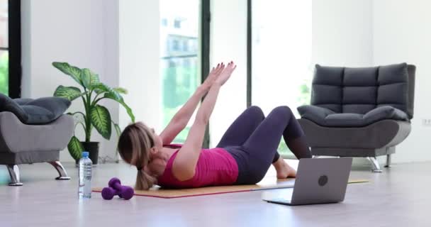 Jonge vrouw trok pers op tapijt thuis kijken videogids op laptop. Online fitness training - Video
