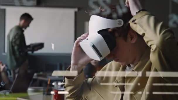 Näkymä lasiseinän läpi nuorten miesten IT-asiantuntija laittaa VR kuulokkeet ja kaukosäätimen testauksen aikana lisätyn todellisuuden sovellus - Materiaali, video