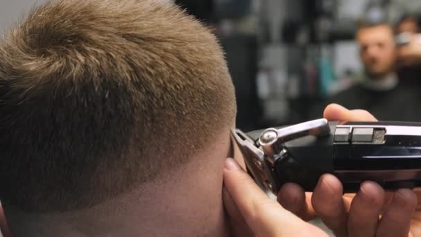 El peluquero experto usa un recortador automático para cortar el cabello del cliente en el templo en el primer plano de la barbería. Peluquería hace peinado elegante por espejo de salón - Metraje, vídeo