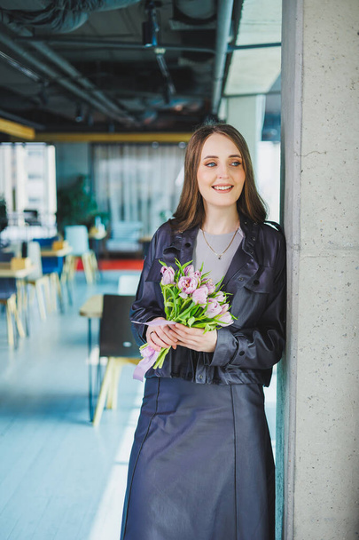 Junge moderne Frau im Büro mit Blumen in den Händen. Tulpen in den Händen einer Frau - Foto, Bild