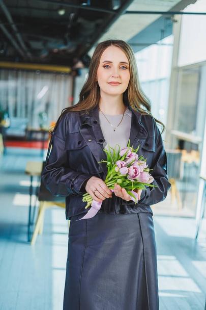 Молодая современная женщина в офисе с цветами в руках. Тюльпаны в руках женщины - Фото, изображение