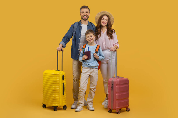 Mężczyzna, kobieta i dziecko stoją obok jasnożółtych i czerwonych walizek. Przygotowują się do podróży lub podróży, żółte tło. - Zdjęcie, obraz