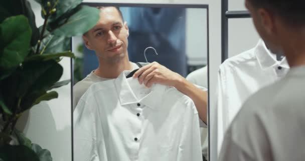 Millennial muž vyzkoušet na košili pánské oblečení obchod zkouší fit a styl v zrcadle. Střední dospělý muž naviguje přes různé možnosti zkoumání mužů módní osoba vybrat oblečení mužské oblečení - Záběry, video