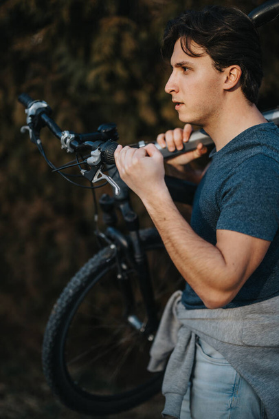 Ένας στοχαστικός άνθρωπος αναπαύεται με το ποδήλατό του στο φόντο ενός καταπράσινου πάρκου, απολαμβάνοντας μια στιγμή ηρεμίας. - Φωτογραφία, εικόνα
