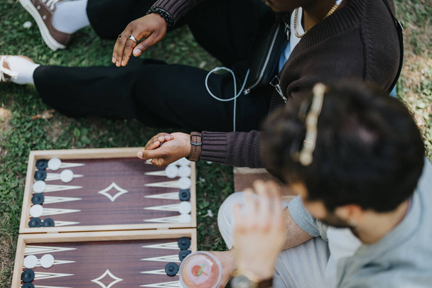 Due amici, provenienti da ambienti diversi, si siedono comodamente all'aperto assecondando un gioco di backgammon spensierato, godendo del calore di una giornata di sole e della gioia di stare insieme. - Foto, immagini