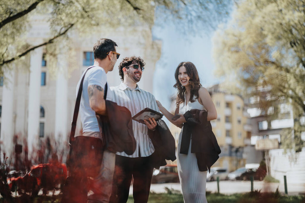 Trois entrepreneurs élégants partagent une discussion joyeuse en plein air dans une ville par une journée ensoleillée, projetant la positivité et le travail d'équipe. - Photo, image