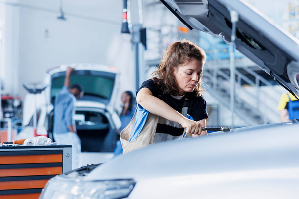 壊れた排気システムを修理する専門の機械用具を使用して車サービスの女性. クライアントの自動車を固定するガレージの熟練したメカニック,最適な自動車性能を確保 - 写真・画像