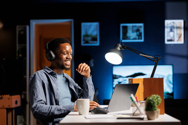Молодой человек обучается дома в режиме онлайн, слушает, как репетитор обсуждает административные вопросы. Африканский американский ученик изучает исполнительный менеджмент и финансы, наслаждаясь подкастом. - Фото, изображение