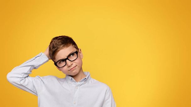 Zweifelhafter Teenager mit Brille, der sich den Kopf kratzt, orangefarbener Hintergrund - Foto, Bild