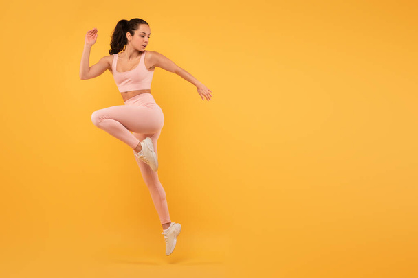 A woman wearing a pink outfit is captured mid-air as she jumps. Her joyful expression is evident as she defies gravity. The background is blurred, emphasizing her movement, copy space - Photo, Image