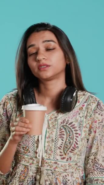 Vídeo vertical Mujer soñolienta bostezando, bebiendo café para ganar energía y deshacerse del dolor de cabeza. Persona agotada sintiéndose fatigada después de la noche sin dormir, bebiendo bebidas con cafeína, fondo del estudio - Metraje, vídeo