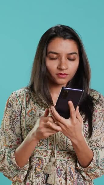 Verticale video Indiase vrouw vegen op smartphone touchscreen te beantwoorden telefoongesprek van vriend, geïsoleerd over studio achtergrond. Portret van persoon die luistert en het eens is met partner tijdens de telefoon - Video
