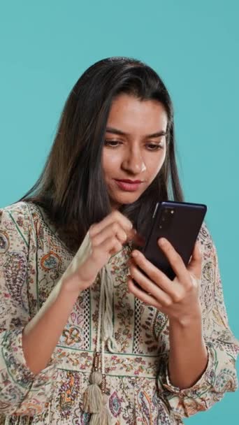 Verticale video Vrouw scrolt graag op het touchscreen van de telefoon om social media feed te controleren, verbaasd door foto. Indiase persoon surfen op internet websites, verbaasd over de inhoud, studio achtergrond, camera A - Video