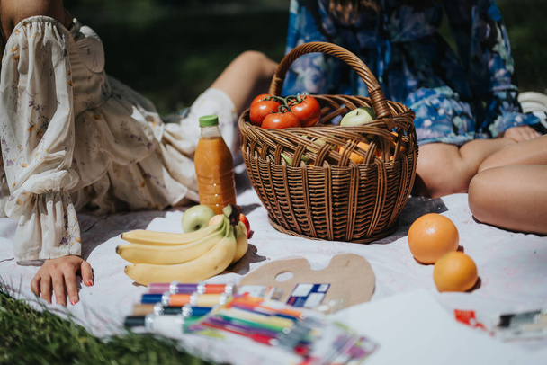 Due sorelle si rilassano in un parco illuminato dal sole, circondate da cibo da picnic e materiale artistico, catturando un momento di gioia e di compagnia. - Foto, immagini