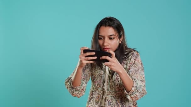 Gracz z rozczarowanym spojrzeniem na twarz po otrzymaniu gry na ekranie, trzymając smartfona. Hinduska kobieta zdenerwowana po utracie gry wideo, gra z telefonu, izolowane na tle studio - Materiał filmowy, wideo