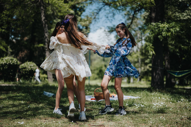 Glückliche und fröhliche Schwestern in Sommerkleidern, die im Kreis in einem üppig grünen Park tanzen und Glück und Jugend ausstrahlen. - Foto, Bild
