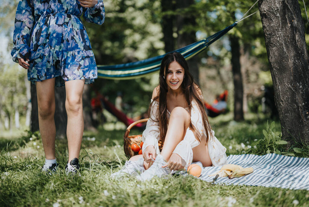 Suorapuheinen hetki vangittiin kaksi sisarta rentoutua puistossa, hymyillen ja nauttien aurinkoinen päivä piknik setup heidän ympärillään. - Valokuva, kuva