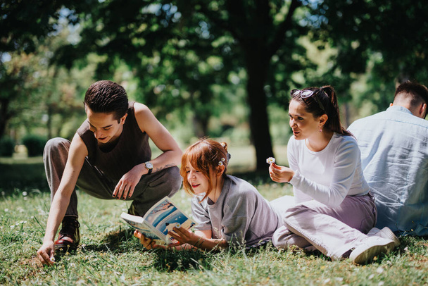 Un groupe de jeunes adultes et un enfant se détendent et s'adonnent à des activités par une journée ensoleillée et lumineuse dans un parc verdoyant. - Photo, image