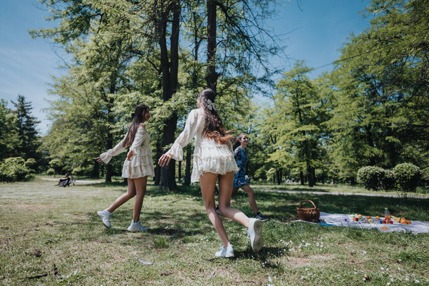 Kolme iloista nuorta naista tyylikkäissä kesämekoissa iloitsevat rehevässä puistossa aurinkoisena päivänä, mikä on esimerkki vapaudesta ja yhdessäolosta viikonlopun retken aikana.. - Valokuva, kuva