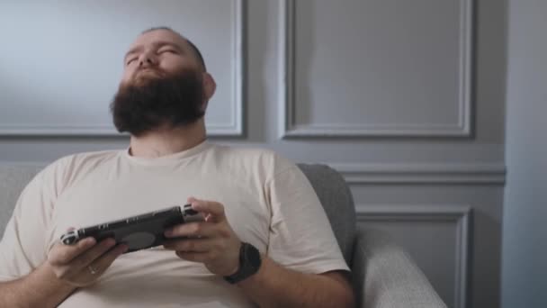 Concept of unhealthy lifestyle. Gadgets addiction. Adult young guy spend his time in video games using tablet. Bearded man celebrating his victory playing portable console, raised fist up when got - Footage, Video