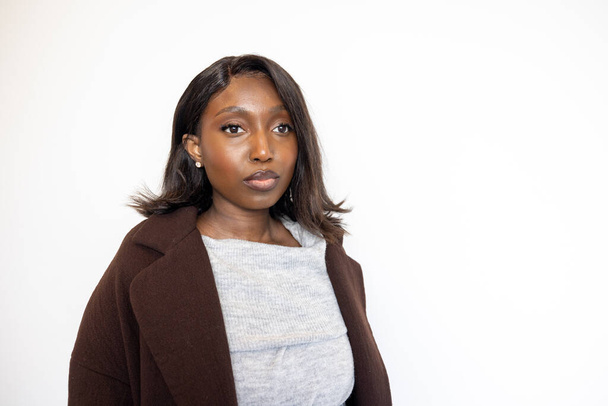 This portrait features a confident young Black woman dressed in stylish winter attire. She wears a gray turtleneck sweater and a dark brown coat, with her dark hair flowing around her shoulders. The - Photo, Image