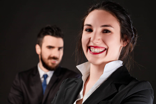 Sonriendo ampliamente, la joven en traje de negocios capta la atención, su colega en el fondo - Foto, Imagen
