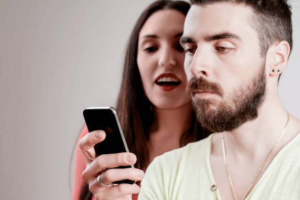 Él sostiene su teléfono de cerca, mientras ella observa, ansioso por leer sus mensajes, destacando una violación de la confianza - Foto, Imagen