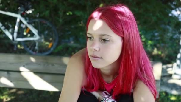 Cámara rastrea a una hermosa joven en forma de fucsia sentado casualmente en un parque de la ciudad - Imágenes, Vídeo