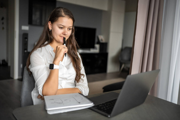Молода жінка використовує ноутбук на домашньому робочому місці, пише нотатки, студентка навчається та дивиться онлайн-вебінар або слухає аудіокурс, концепцію освіти електронного навчання. Високоякісна фотографія - Фото, зображення